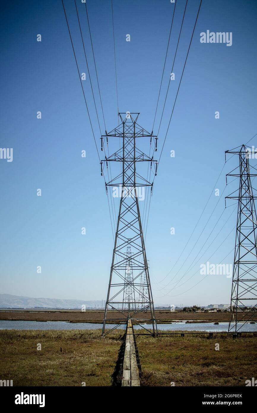 Pilón de electricidad centrado en la imagen con cables de potencia paralelos que van a ella y torres sucesivas que parecen más pequeñas, en la distancia. Foto de stock