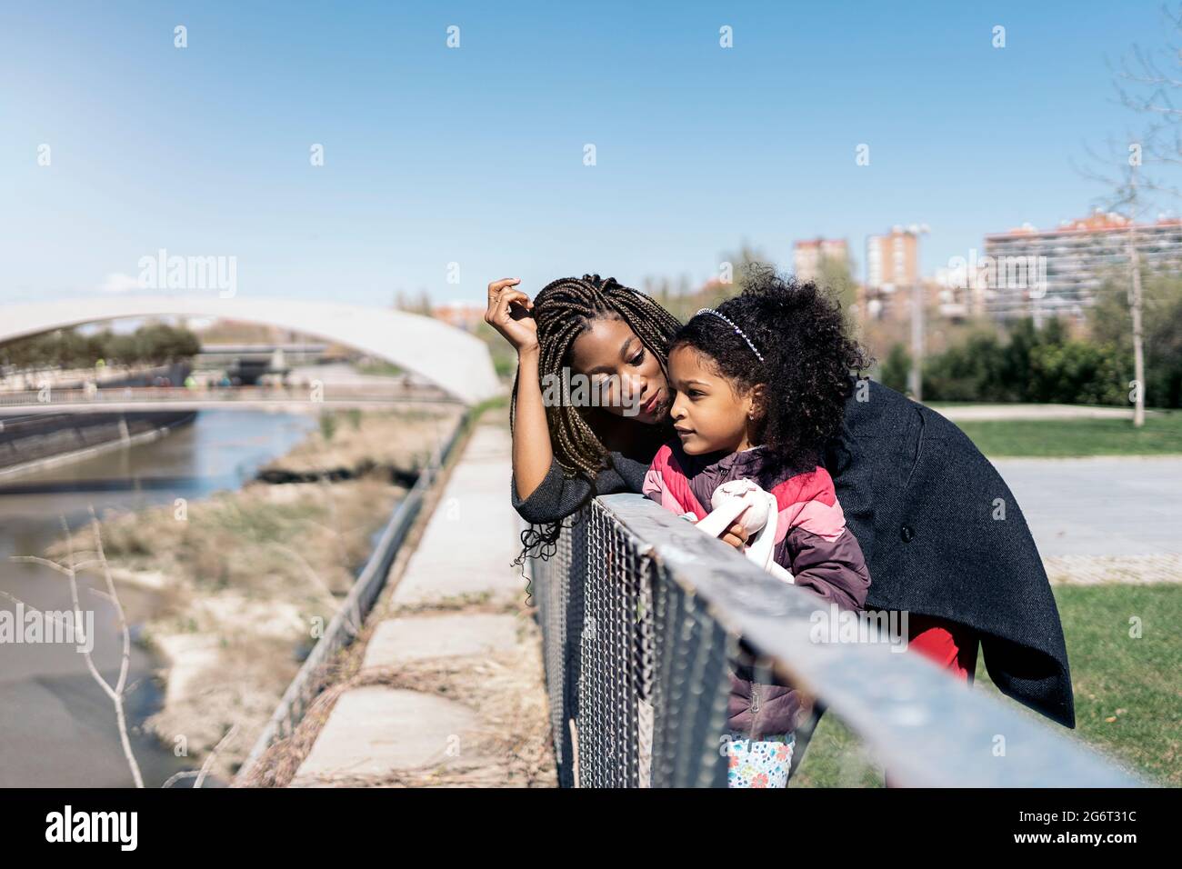 Mujer africana pasando el día soleado de primavera en el parque con su hija pequeña. Están mirando al río. Foto de stock