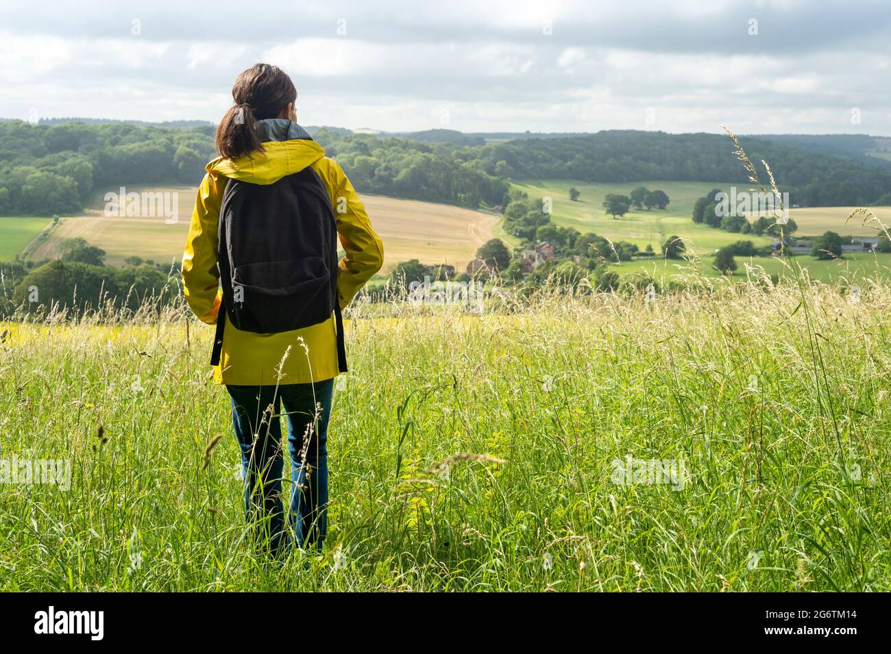 Caminadora mujer con chaqueta amarilla y una mochila disfrutando de la vista del campo con vistas a los Sussex Downs. Foto de stock