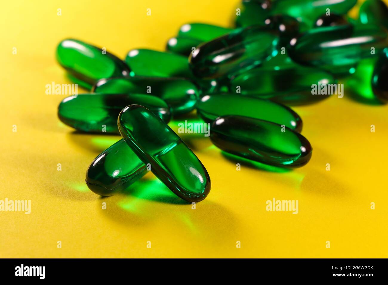 Cápsulas verdes de la píldora del aceite esencial en amarillo brillante Foto de stock