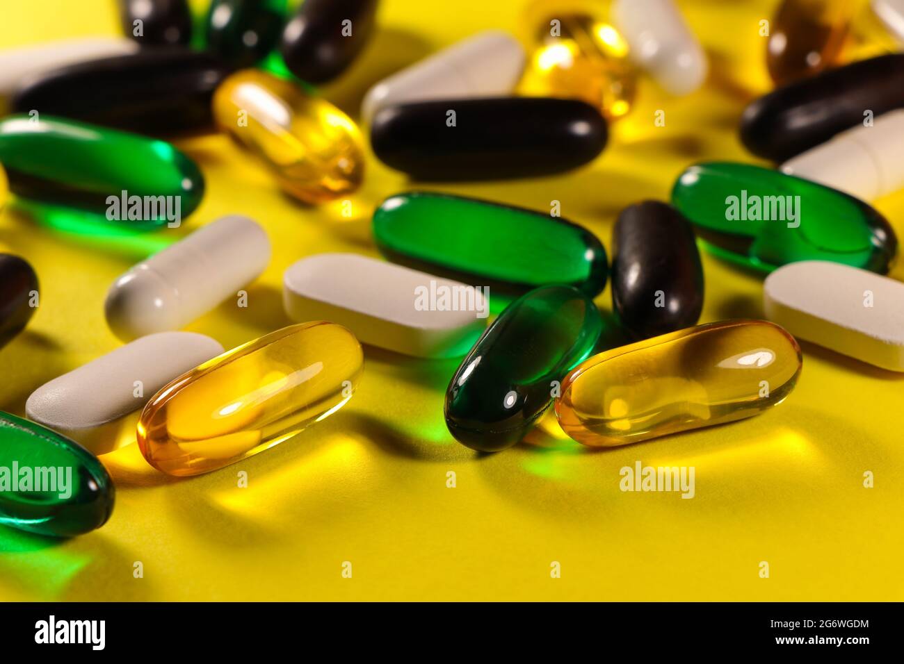 Variedad de píldoras y cápsulas sobre superficie amarilla brillante Foto de stock