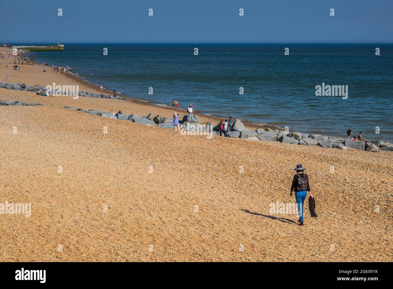 Una mujer caminando a lo largo de la playa con otras personas en el fondo. Tomado en la playa en Hastings, Reino Unido, sureste de Inglaterra. Foto de stock