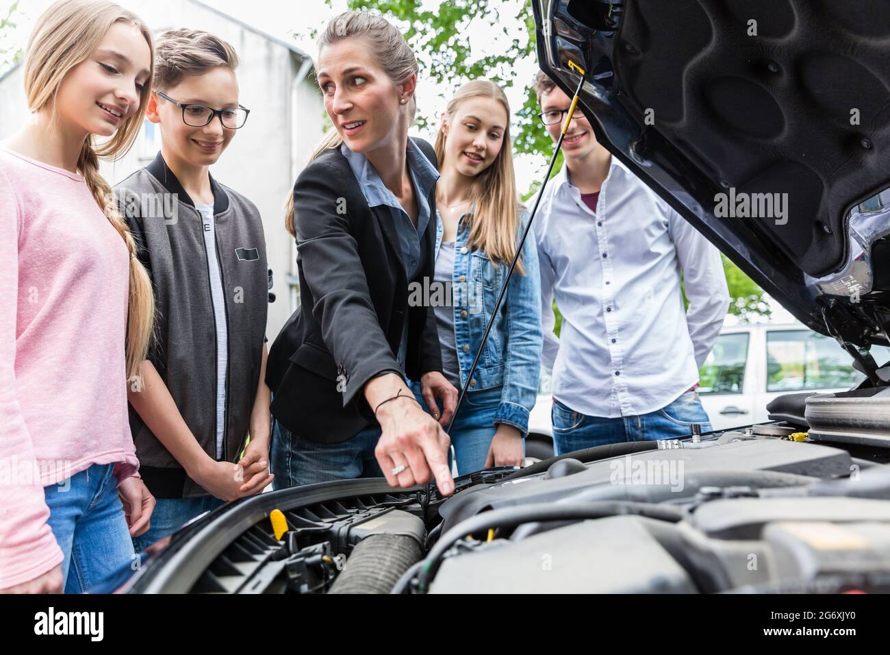 Profesor de conducción clase mostrando el motor del coche, lo que les permite mirar debajo del capó Foto de stock