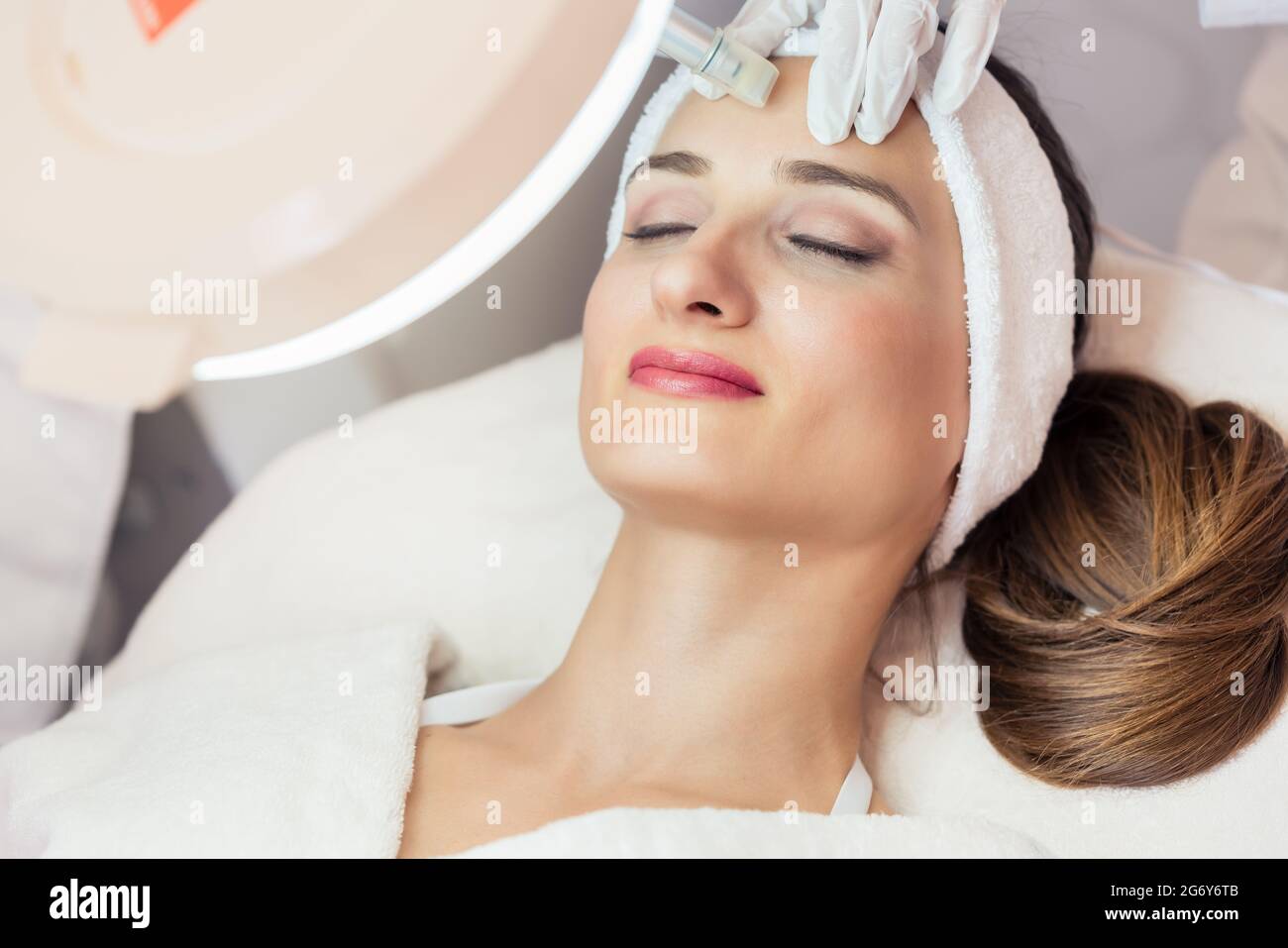 Primer plano de la cara de una mujer que se relaja durante un tratamiento de estiramiento facial no quirúrgico en un salón de belleza contemporáneo con tecnología innovadora Foto de stock