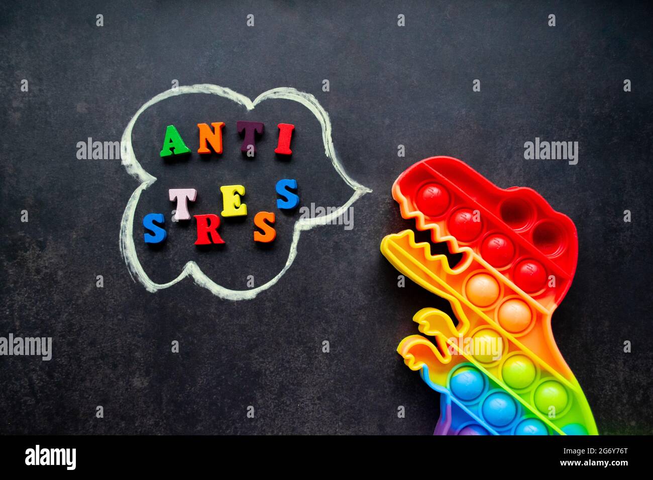 Juguete pop que dinosaurio arco iris colores sobre un fondo negro con letras multicolores y la inscripción-Anti-estrés en una burbuja de voz. Foto de stock