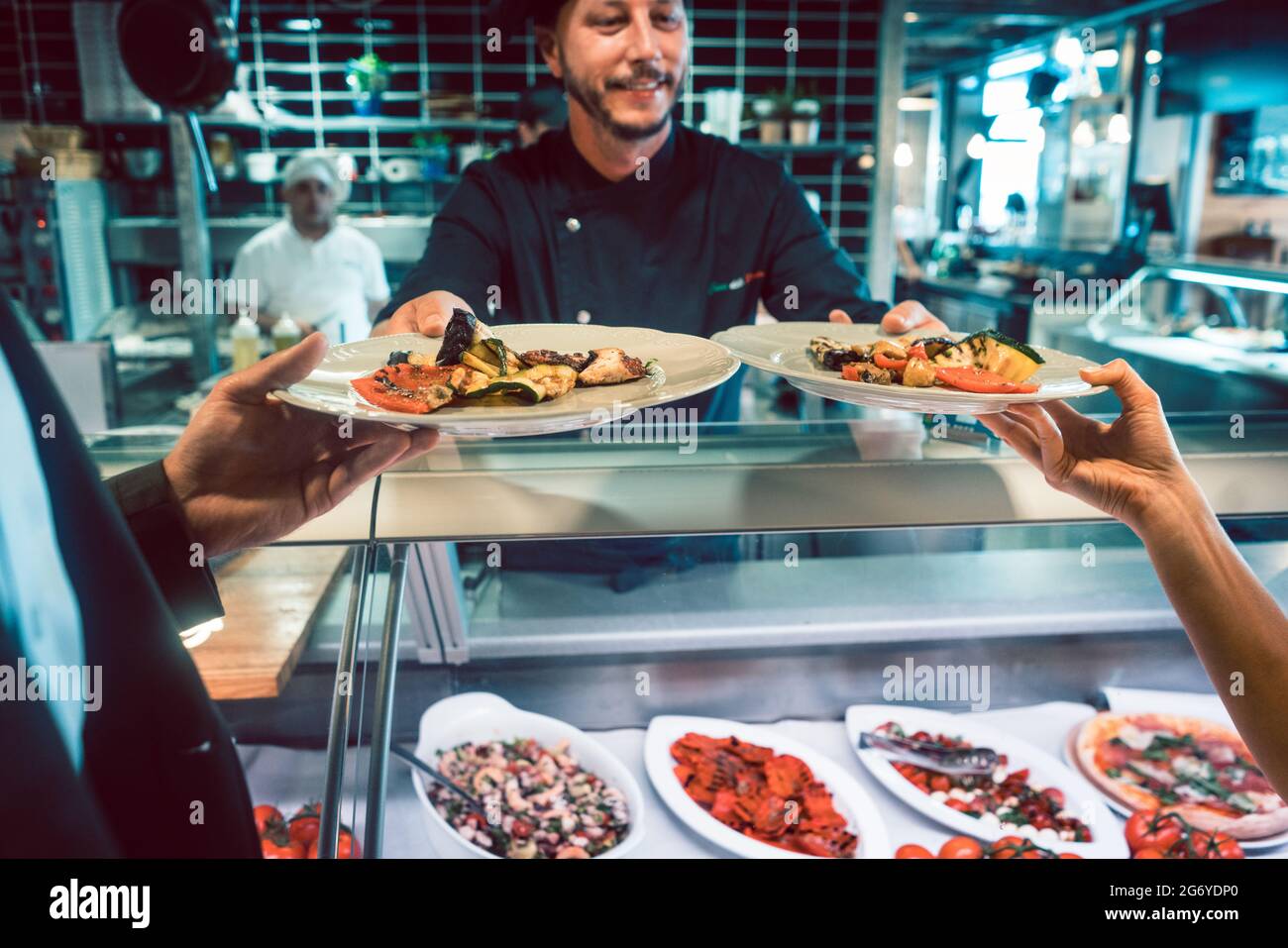 Primer plano de dos platos con mariscos y deliciosas verduras, servidos por un chef experimentado a una pareja en el mostrador de un restaurante de moda con fre Foto de stock