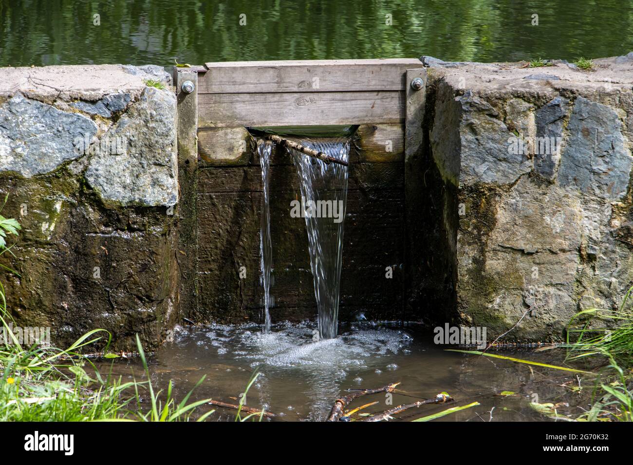 Un agua fluye a través de las esclusas en la pequeña presa de piedra del estanque Foto de stock