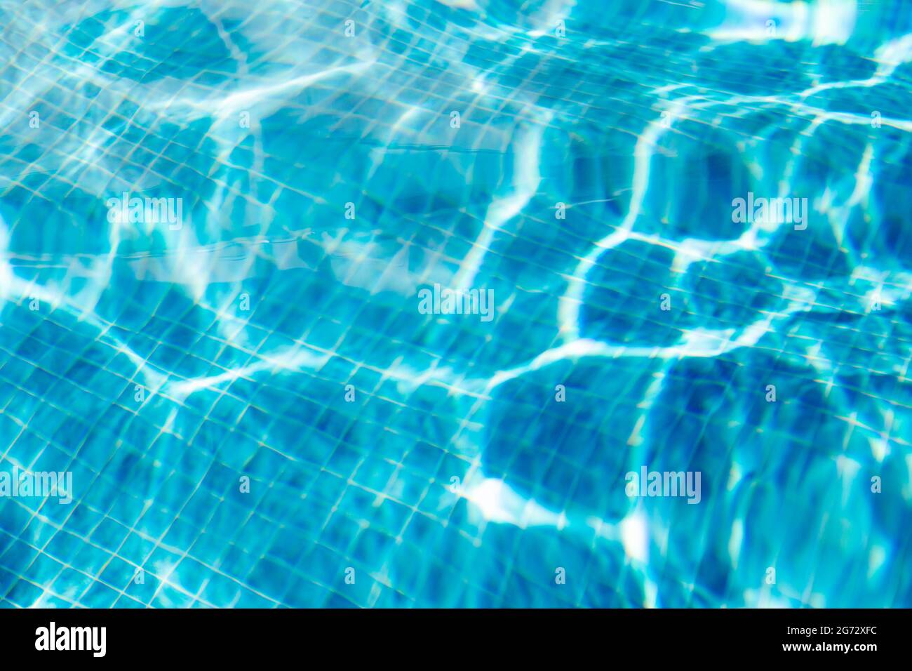 Piso de una piscina que refleja rayos de sol en azulejos cuadrados azules. Foto de stock