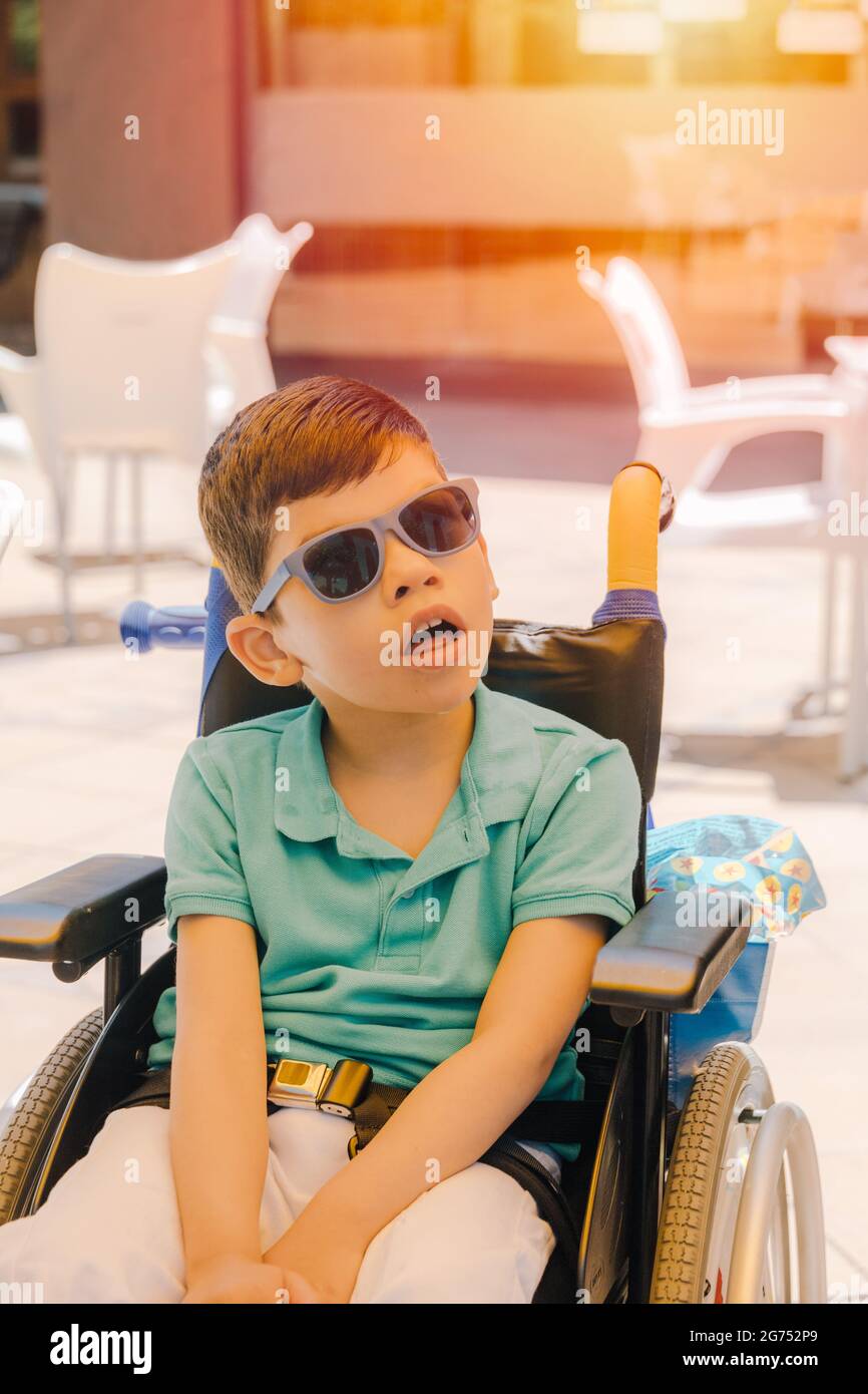 Niño con discapacidad neurosívica del síndrome de Pitt-Hopkins en silla de  ruedas con gafas de sol y boca abierta en un día de verano Fotografía de  stock - Alamy
