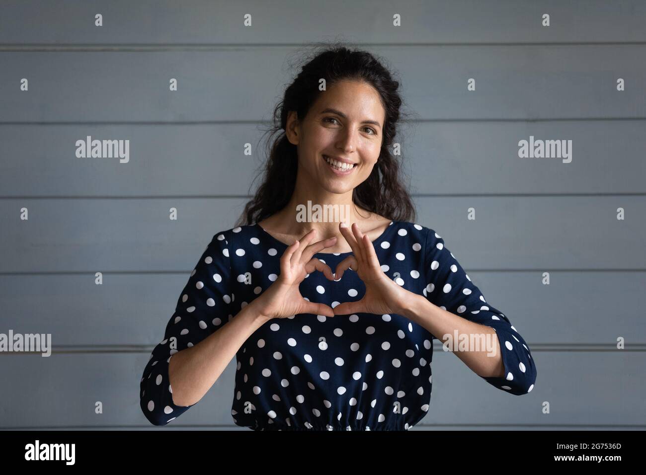 Feliz y agradecida mujer hispana milenaria mostrando gesto de amor Foto de stock