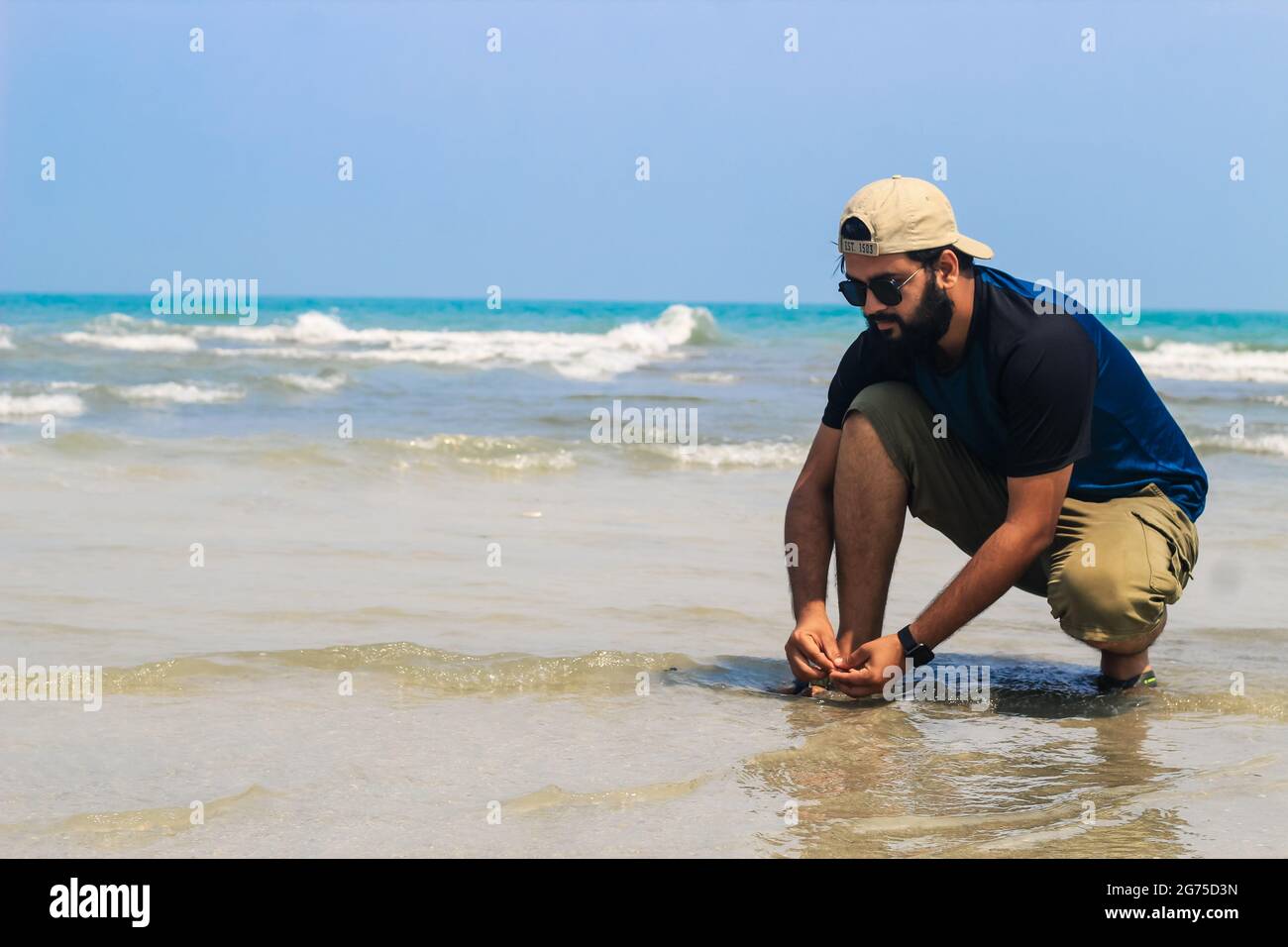 El joven junto al mar recoge conchas marinas en la playa. Puesta de sol, vacaciones de verano en el mar o en el océano. Un niño en la playa recogiendo conchas. Foto de stock