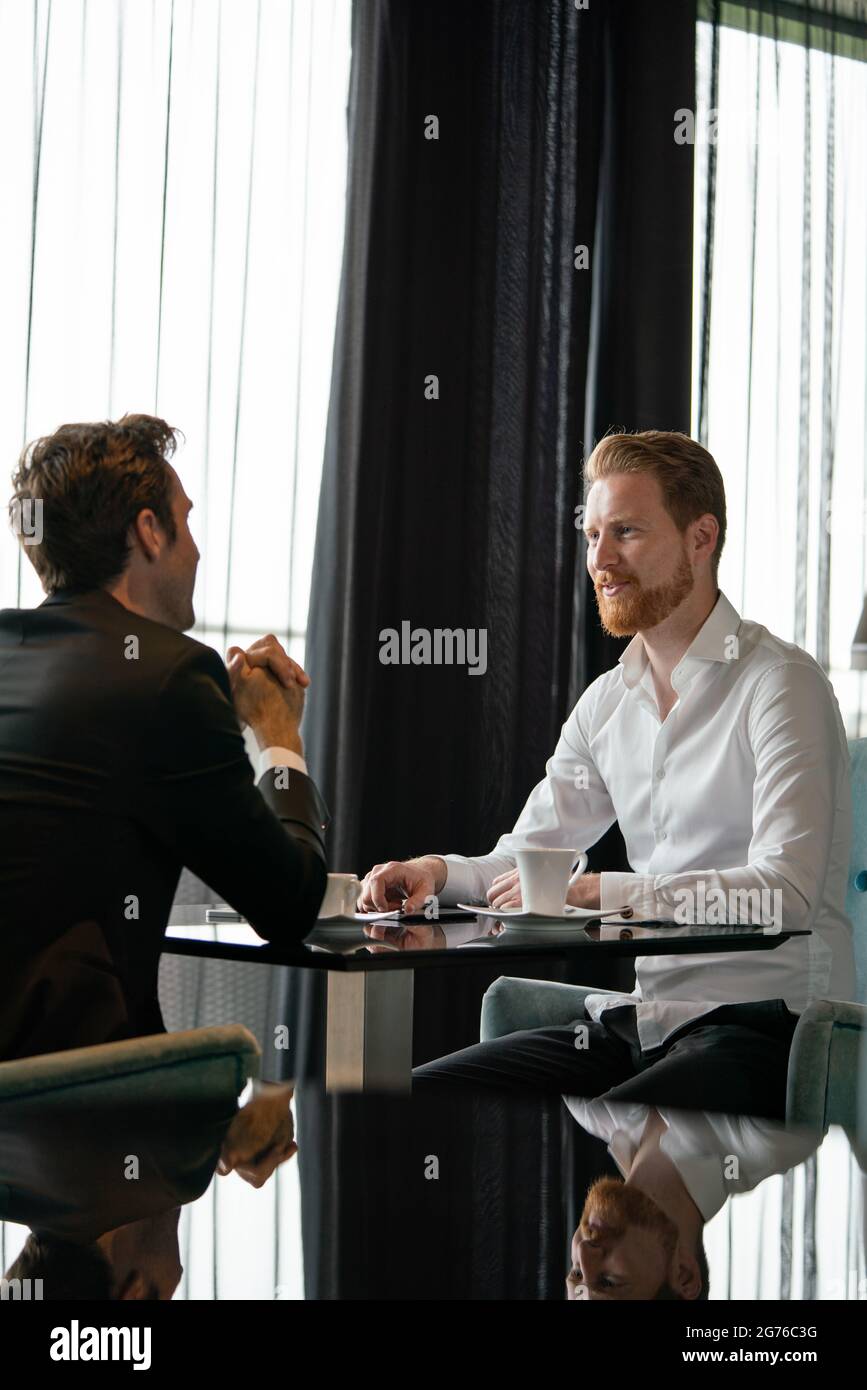 Exitoso empresario sonriendo mientras discutía con su pareja durante la reunión en coffee break Foto de stock