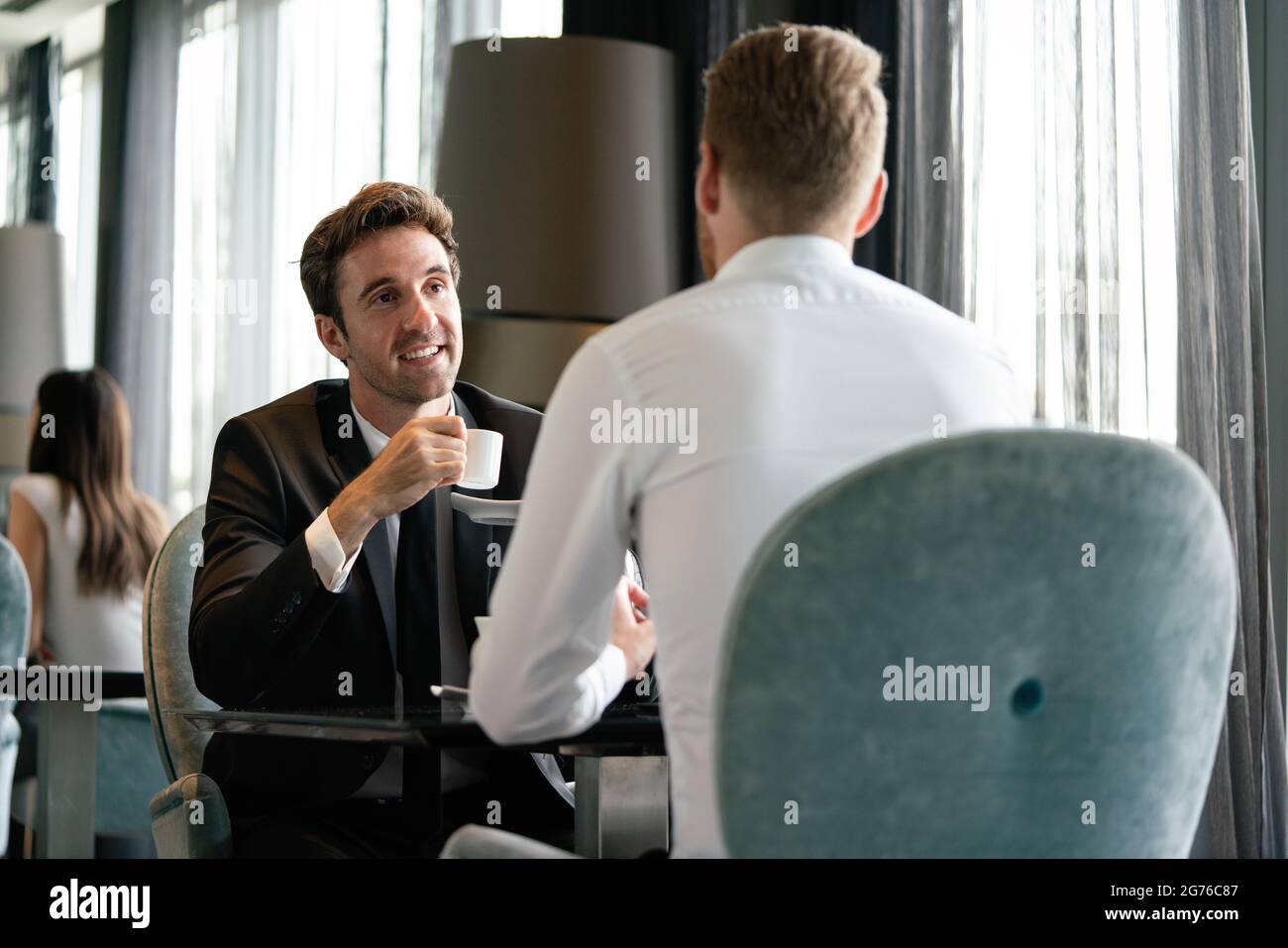 Exitoso empresario sonriendo mientras discutía con su pareja durante la reunión en coffee break Foto de stock