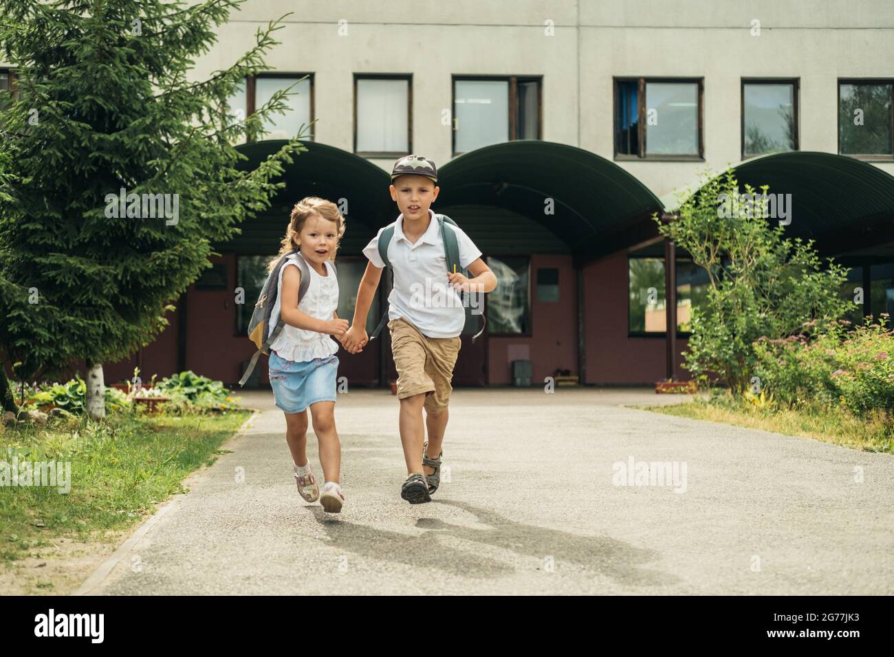 Dos niños caucásicos, niño y niña, corriendo de la escuela con bolsas detrás de sus espaldas y libros. Regreso a la escuela. Foto de stock