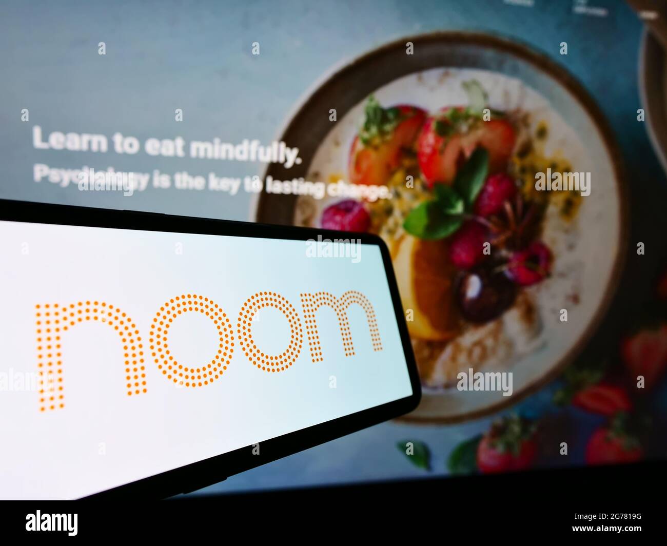 Smartphone con el logotipo de la empresa de plataformas de pérdida de peso de EE. UU. Noom Inc. En pantalla frente al sitio web de la empresa. Enfoque en la parte central derecha de la pantalla del teléfono. Foto de stock