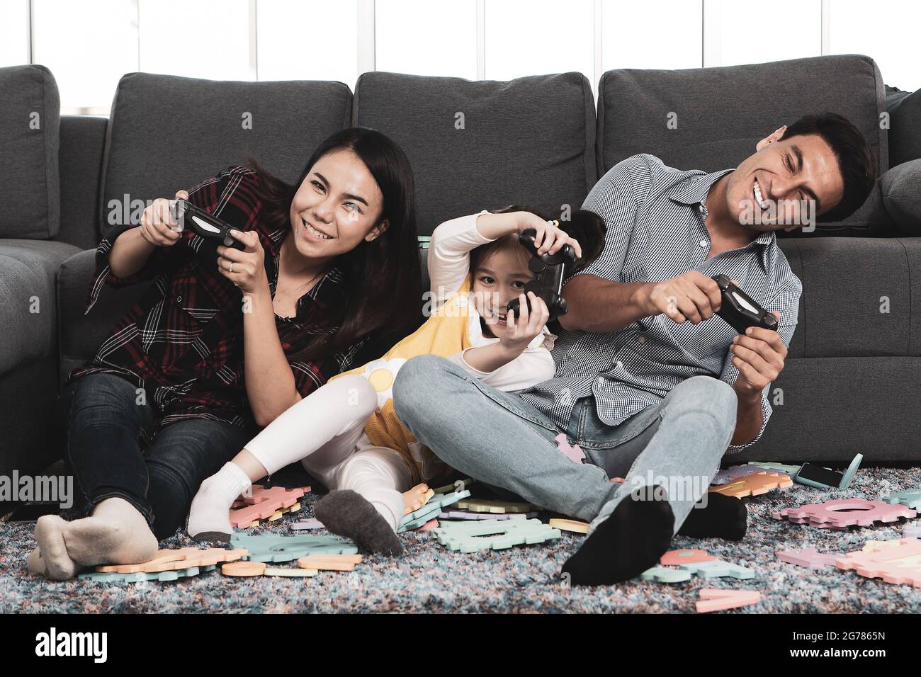 Marido caucásico y esposa asiática con media raza linda hija feliz familia compartir tiempo en casa, sosteniendo el mando del juego y jugando junto con exc Foto de stock