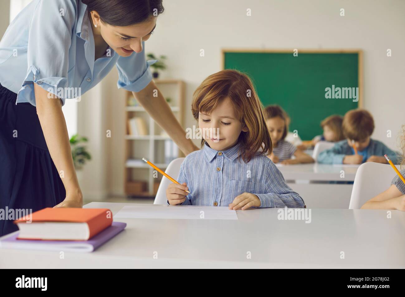 La estudiante de escuela primaria en clase hace una asignación escolar con la ayuda de una maestra. Foto de stock