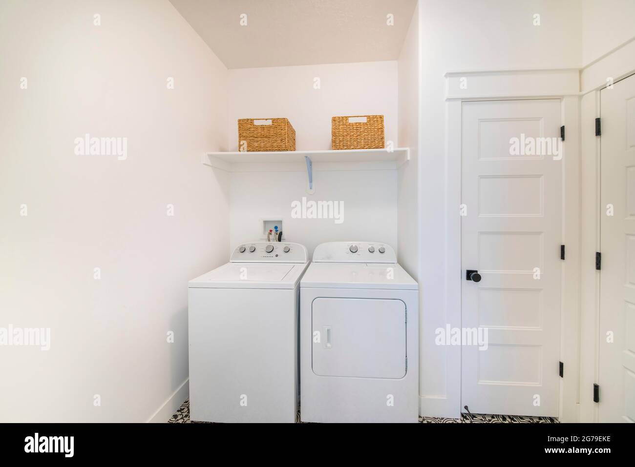 Pequeño cuarto de lavandería blanco interior con lavadora secadora al lado de una puerta blanca Fotografía de stock - Alamy