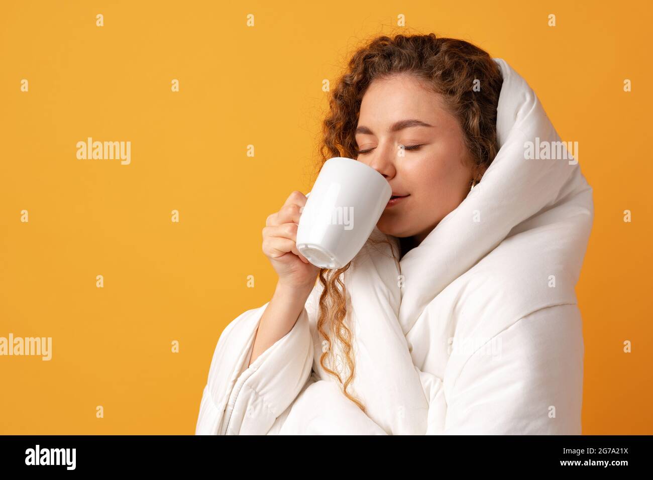 Mujer joven adormecida con pelo rizado cubierto de manta y sosteniendo una  taza de café sobre fondo amarillo Fotografía de stock - Alamy