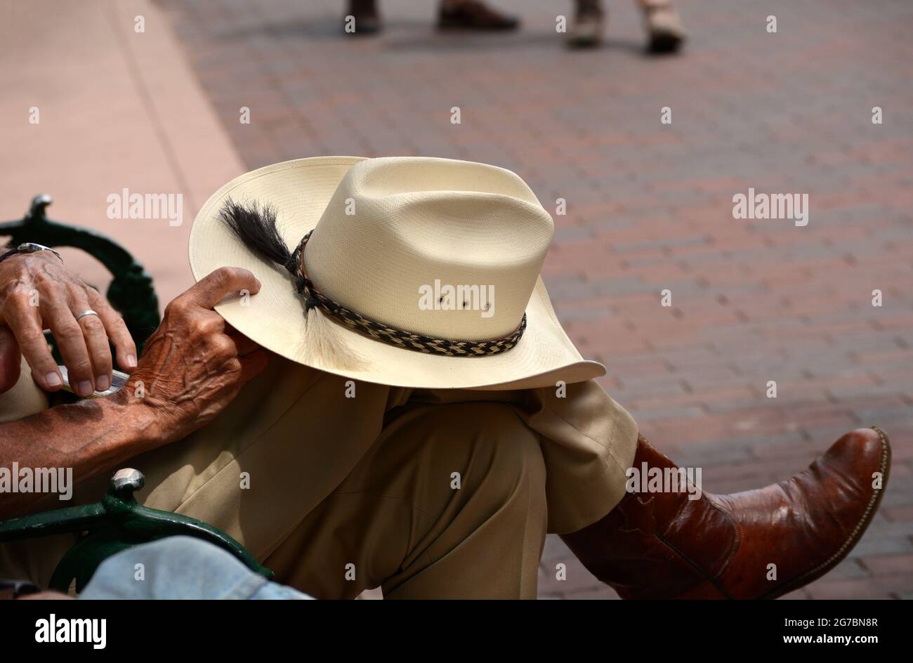 Un hombre con botas de vaquero y un sombrero de vaquero Stetson de paja se relaja en un banco parque en Santa Fe, México de stock Alamy