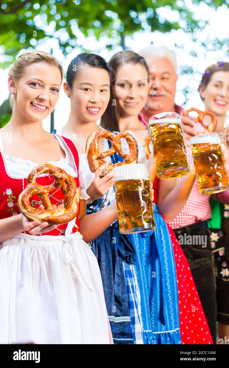 En el jardín de la cerveza - amigos, el hombre y la mujer en el Tracht, Dirndl y Lederhosen bebiendo una cerveza fresca en Baviera, Alemania Foto de stock