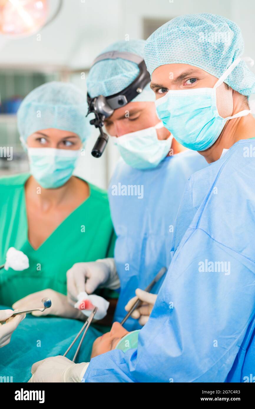 Hospital - equipo médico de cirugía en la sala de operaciones o teatro de la clínica que opera en el paciente, tal vez es una emergencia, asistente que sostiene un algodón Foto de stock