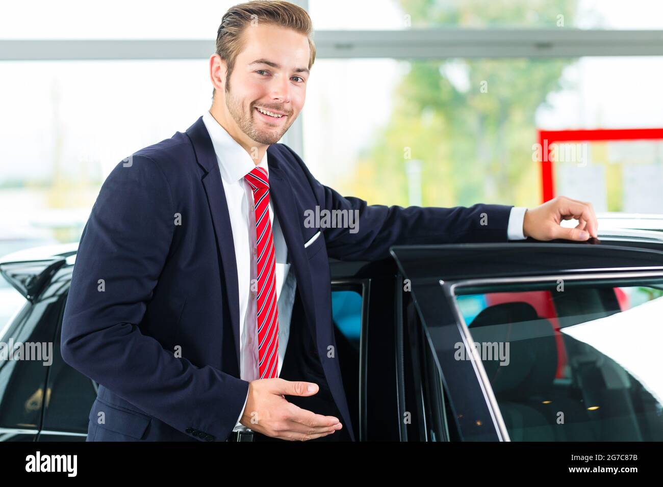 Vendedor o vendedor de coches en concesionario de coches con la llave de presentar sus autos nuevos y usados en el showroom Foto de stock