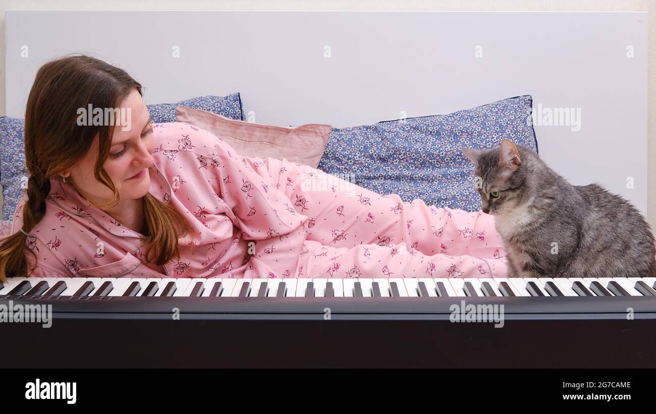 Feliz mujer en pijamas rosa y un gracioso gato aprender a tocar el piano en  una cama de casa Fotografía de stock - Alamy
