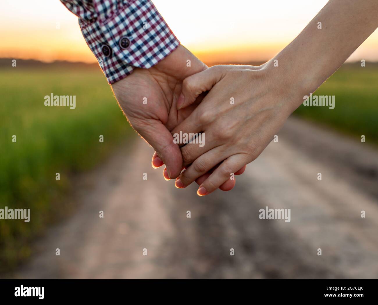 Concepto de amor. Una pareja sosteniendo la mano durante la puesta de sol,  un símbolo de amor y relación feliz. Una joven pareja enamorada camina a  través de un campo al atardecer,