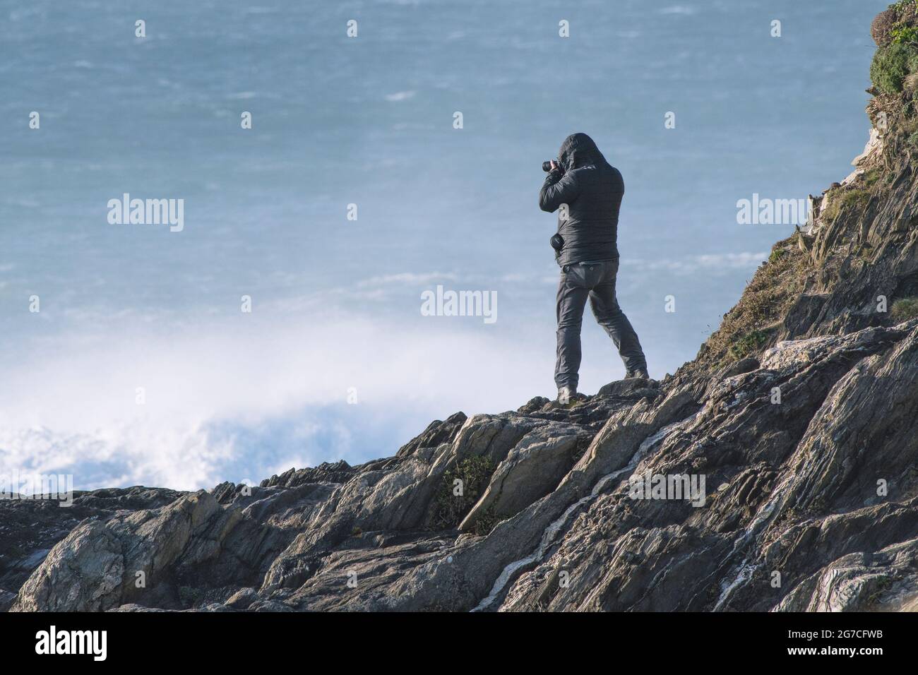 Un hombre tomando fotografías de una posición precaria en las rocas de Towan Head en Newquay en Cornwall. Foto de stock