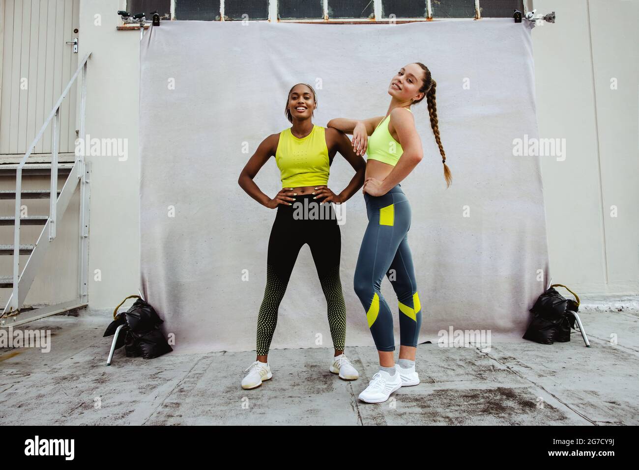 Dos mujeres con ropa de fitness mirando la cámara en la azotea después de  la sesión de entrenamiento. Atletas mujeres relajándose después de hacer  ejercicio en la terraza del edificio Fotografía de