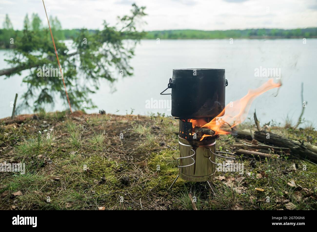 El cornamenta con comida para cocinar está sobre un quemador portátil de metal desde el que hay una llama, de la madera quemada, sobre una roca. Foto de stock