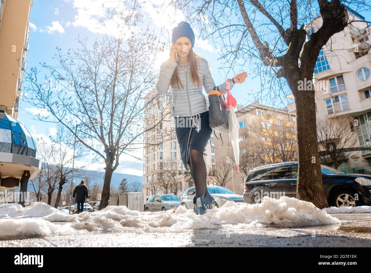 Mujer caminando por el derretimiento de la nieve en invierno habla por teléfono Foto de stock