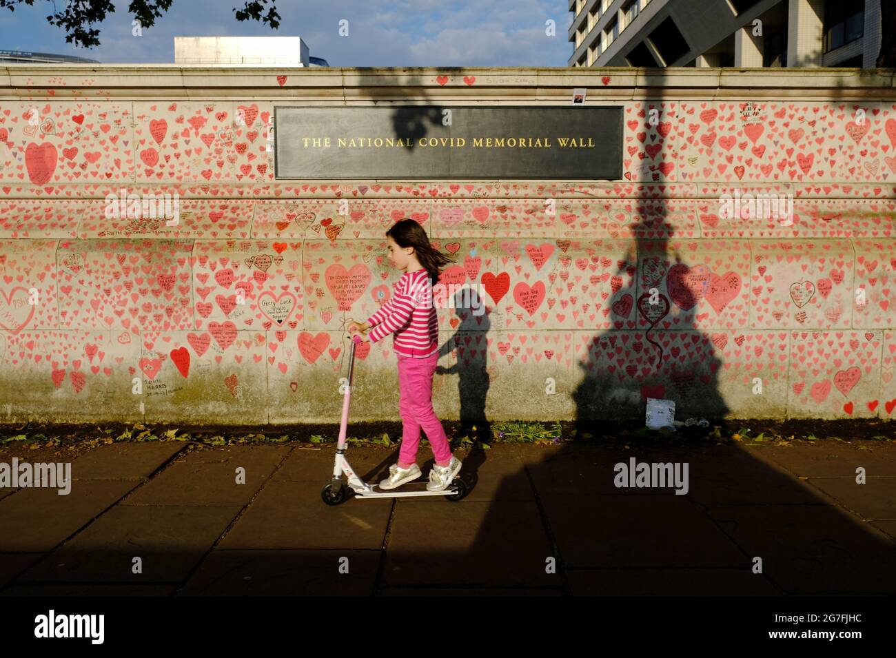Una joven que monta en scooter pasa por el National Covid Memorial Wall en el Southbank de Londres, cerca del St Thomas' Hospital. Foto de stock