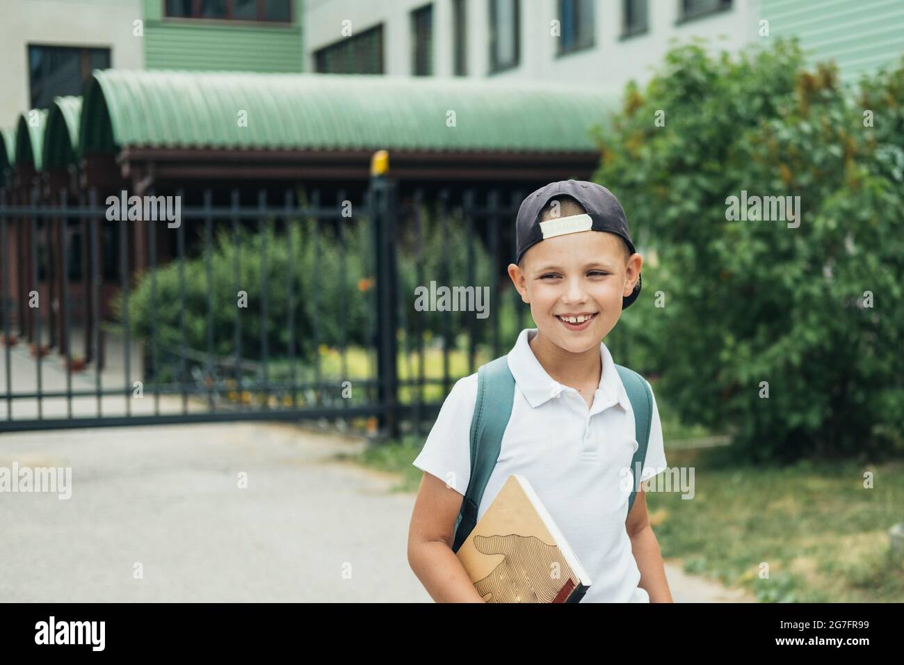Niño sonriente, estudiante de escuela primaria, caminando a la escuela con bolsa detrás y libro. Los estudiantes están listos para el nuevo año. Regreso a la escuela. Foto de stock