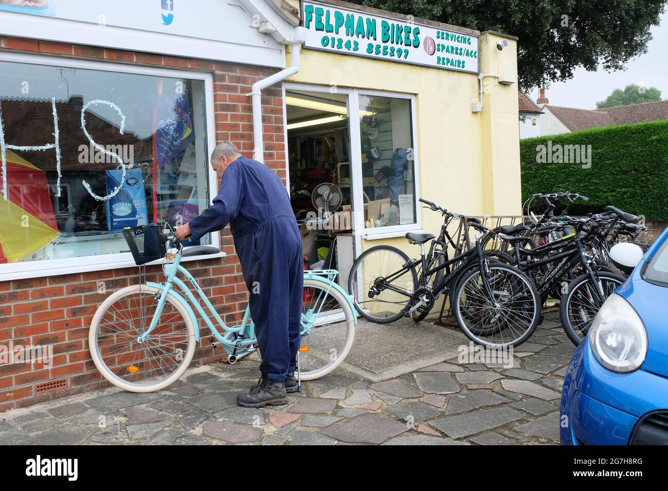 Hombre de reparación de bicicletas fuera de su taller comprobando sobre una bicicleta de ciudad verde pálido Foto de stock