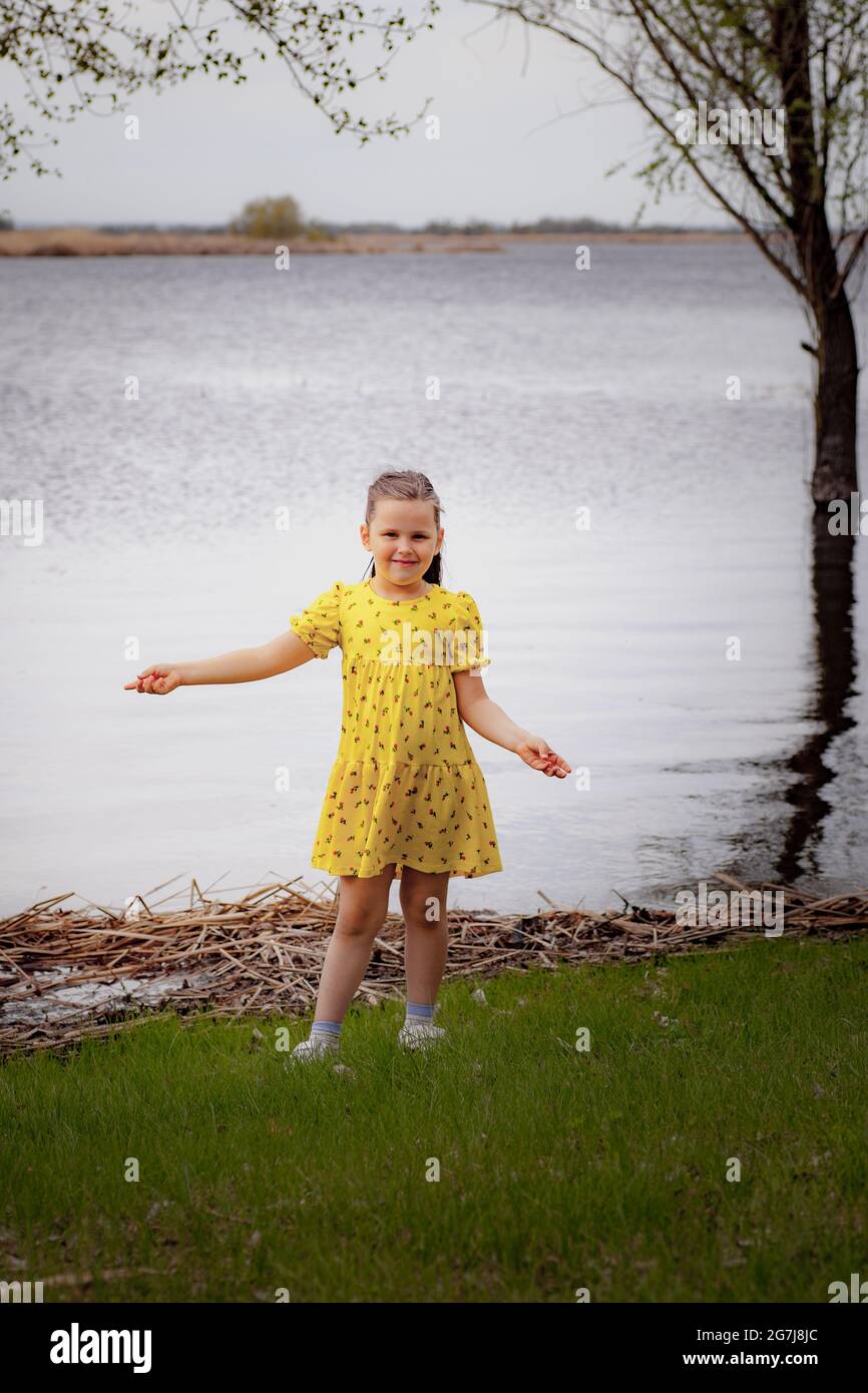 estilo de vida retrato completo de una chica con un vestido amarillo en la orilla del río disfrutando de un cálido día de primavera, césped verde y un viaje local Foto de stock