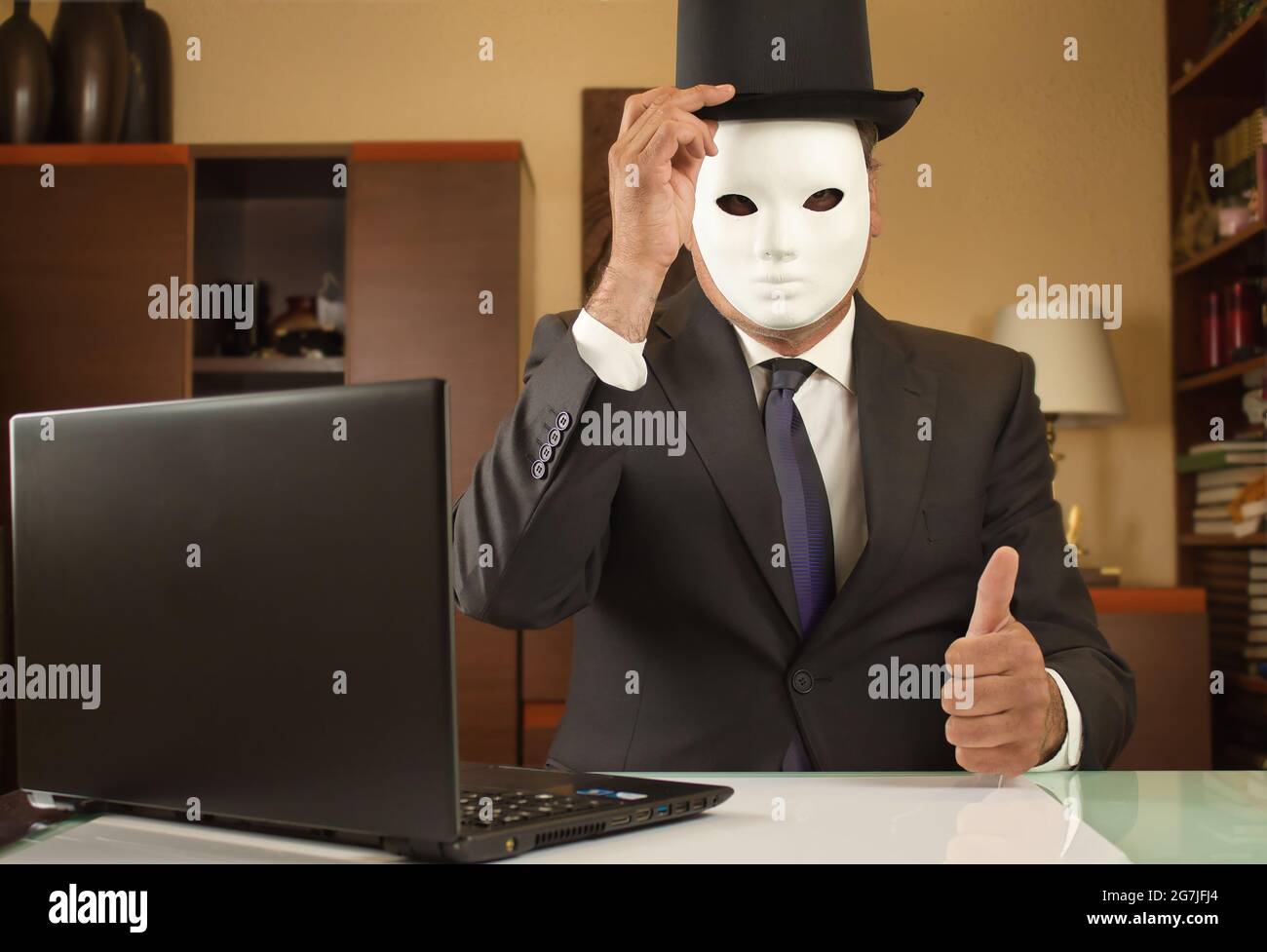 el empresario camuflado con una máscara y un sombrero saluda y teletrabajo desde casa debido a restricciones covid Foto de stock