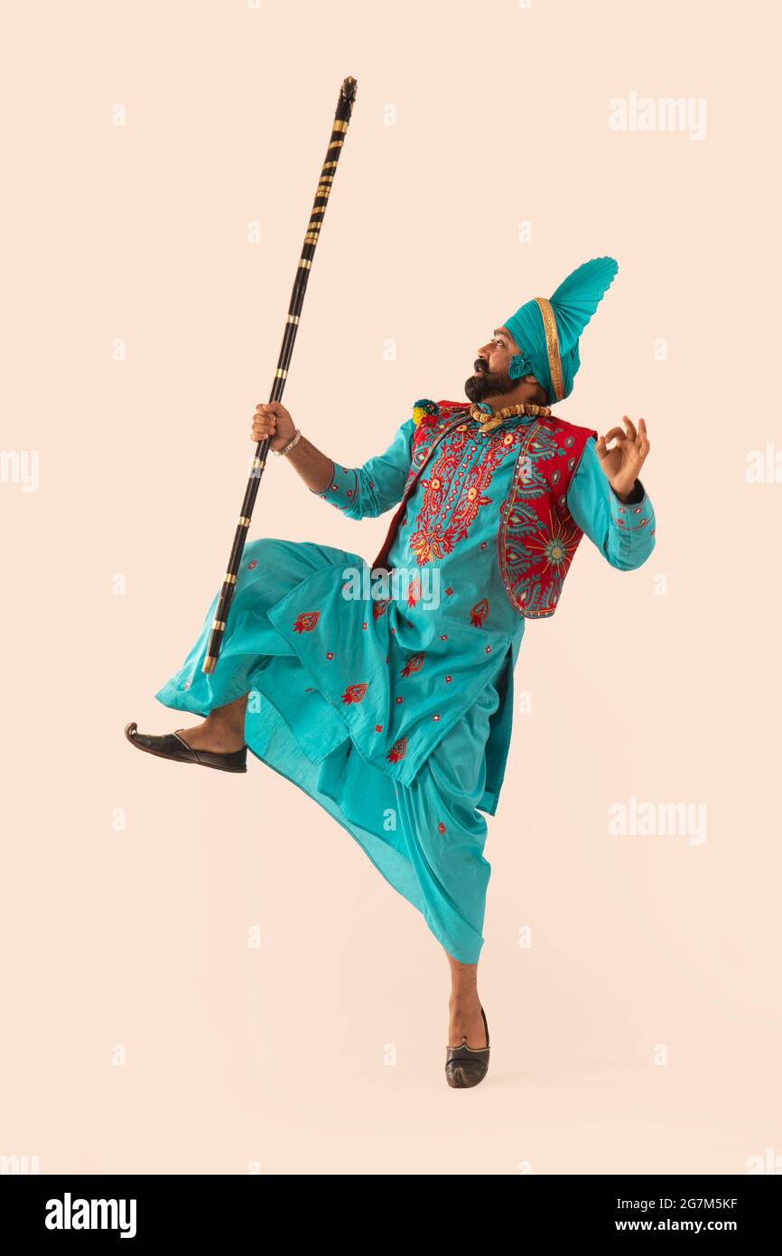 Un Bhangra Dancer frente a la izquierda realizando un paso de baile con una pierna elevada y Khunda en la mano. Foto de stock