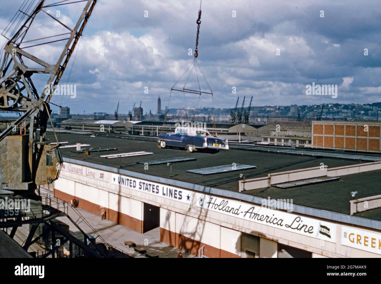 Transporte en automóvil en barco en los muelles del río Hudson en los muelles de Hoboken, Nueva Jersey, EE.UU. A finales de 1950s – aquí se suspende un coche en el aire en su viaje transatlántico. La señalización indica que las instalaciones de almacenamiento en tierra incluyen a las compañías navieras Cunard Line, United States Lines y Holland-America Line. Esta imagen proviene de una antigua transparencia de color amateur de Kodak, una fotografía vintage de 1950s. Foto de stock