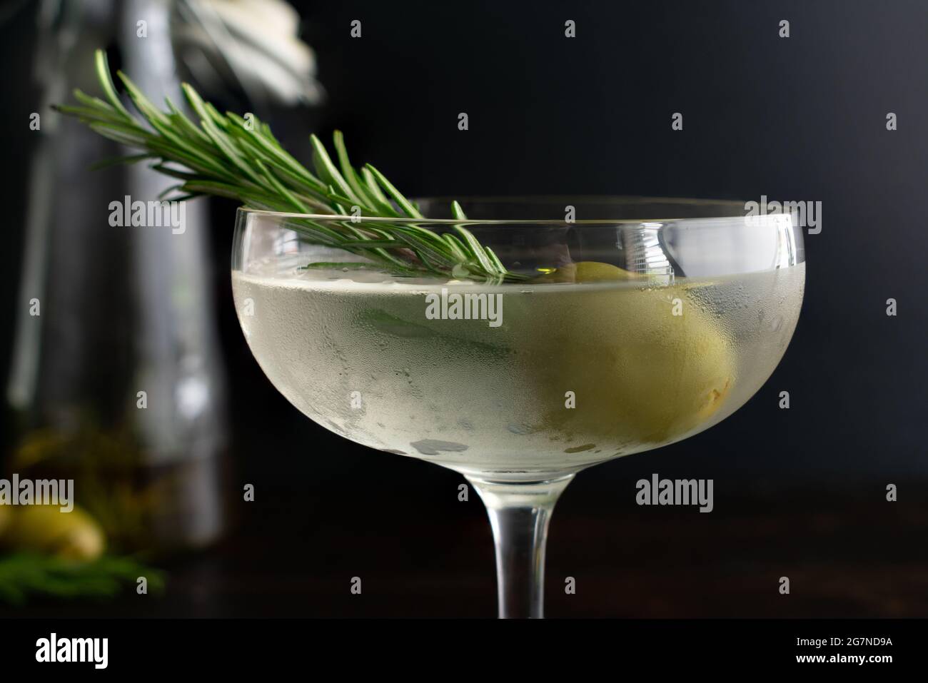 Aceite de romero ahumado Martini sucio: Un martini de ginebra sucio servido en un vaso coupé y adornado con una ramita de romero en una oliva verde Foto de stock