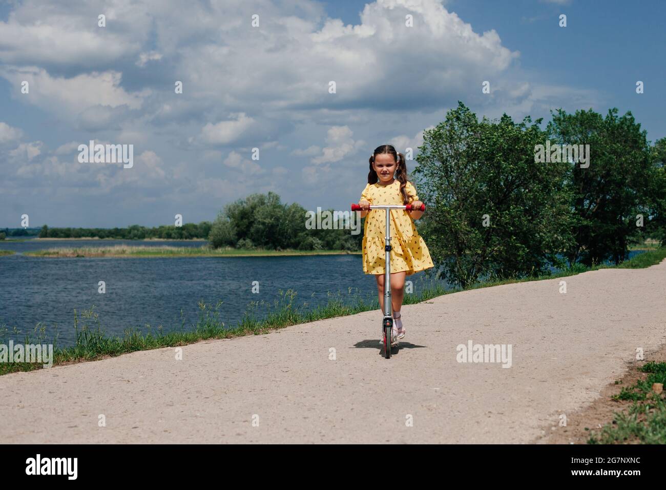 una niña en un scooter, un fin de semana familiar en un mini viaje local, un scooter infantil como símbolo de la actividad familiar y la nueva normalidad Foto de stock