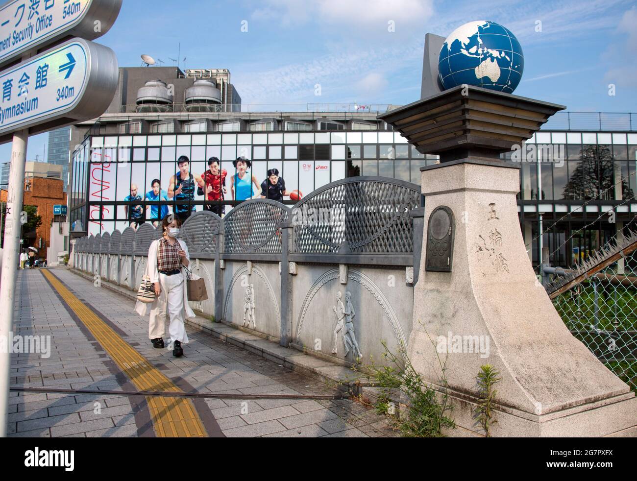 Los peatones pasan por el puente olímpico cerca del parque Yoyogi, Tokio, el 21 de junio de 2021. Mientras que el puente formaba parte de un nuevo sistema de carreteras construido antes de los Juegos Olímpicos de 1964, los globos terráqueos sobre los pilares y relieves de piedra de temática olímpica se añadieron más de 25 años después. Robert Gilhooly foto Foto de stock