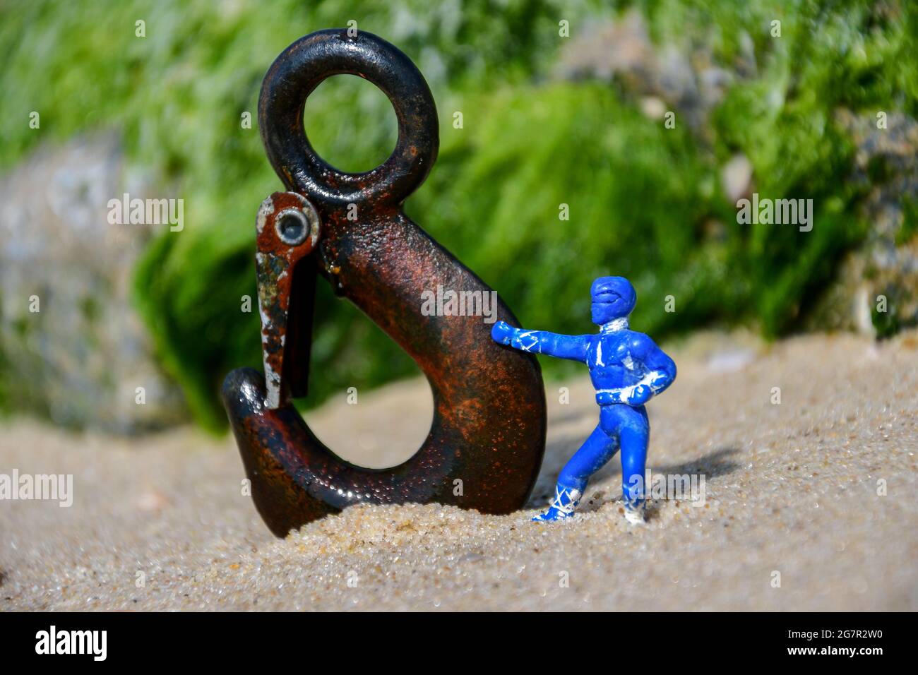 Figurilla de plástico azul con un brazo extendido tocando un gancho de metal plantando en la arena en una playa Foto de stock