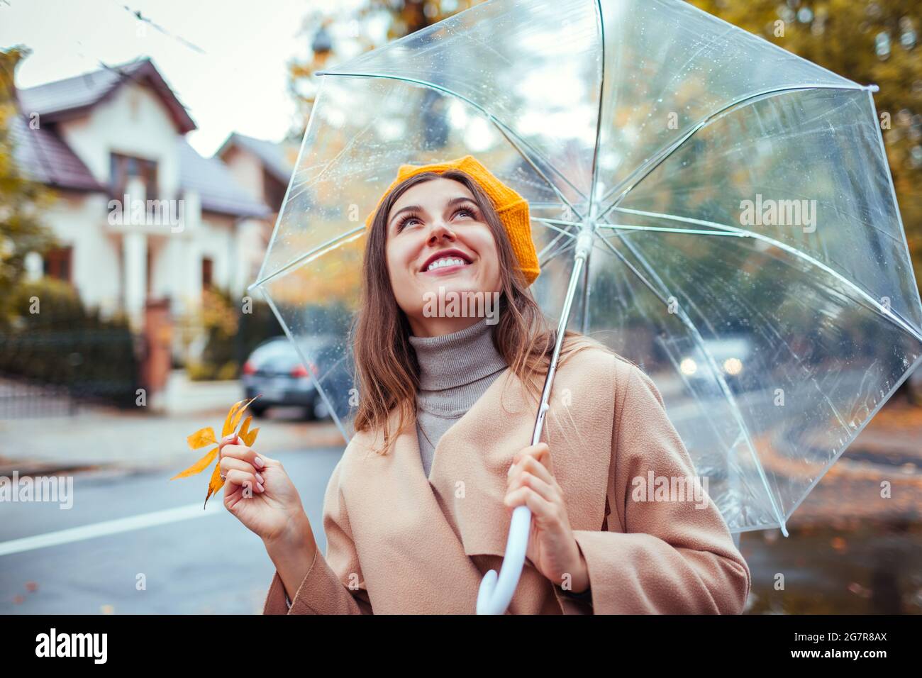 Feliz mujer joven al aire libre bajo paraguas transparente durante la lluvia sosteniendo hojas amarillas. Chica estilo con ropa y accesorios de abrigo. FA Fotografía de stock - Alamy