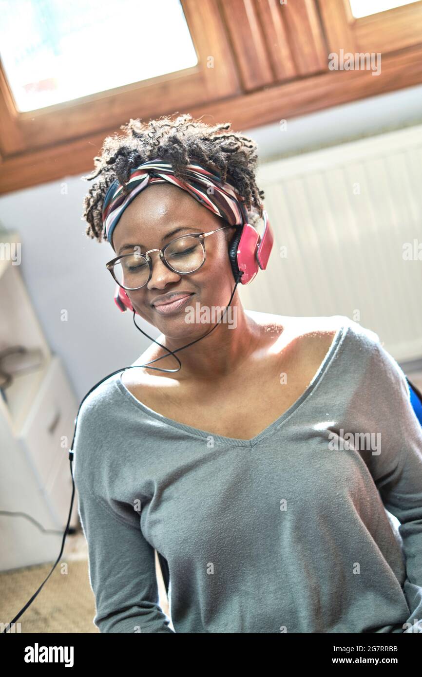 Mujer negra joven con peinado afro escuchando música con auriculares en el interior de una casa. Concepto de estilo de vida. Foto de stock