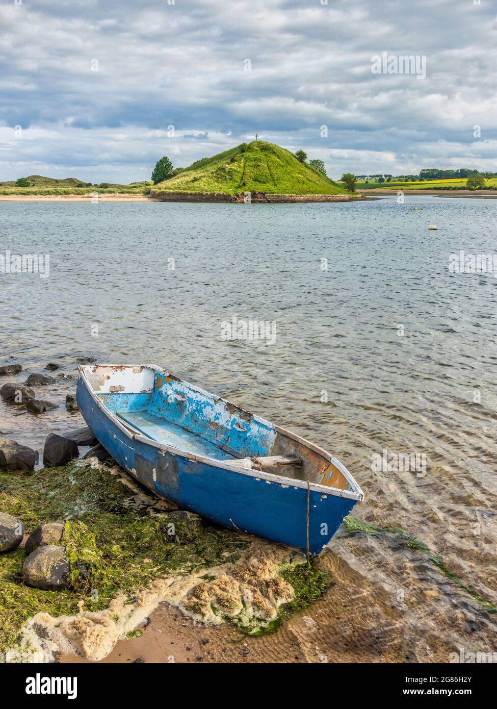Un viejo bote azul de remo amarrado en el estuario del ALN en Alnmouth con Church Hill al fondo, Northumberland, Inglaterra, Reino Unido Foto de stock