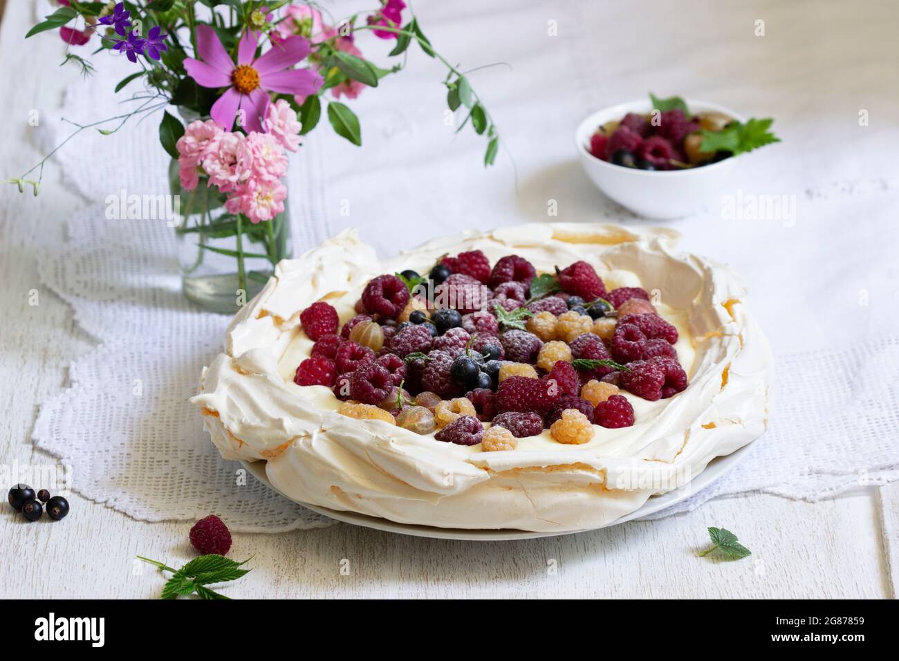 Pastel de Pavlova con crema y bayas y un ramo de flores sobre un fondo claro. Foto de stock