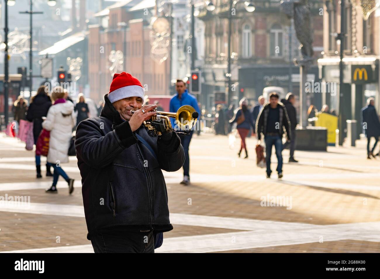 Un hombre con un sombrero de Navidad del Padre tocando la trompeta en una calle peatonal en Leeds, West Yorkshire, Inglaterra, Reino Unido. Foto de stock