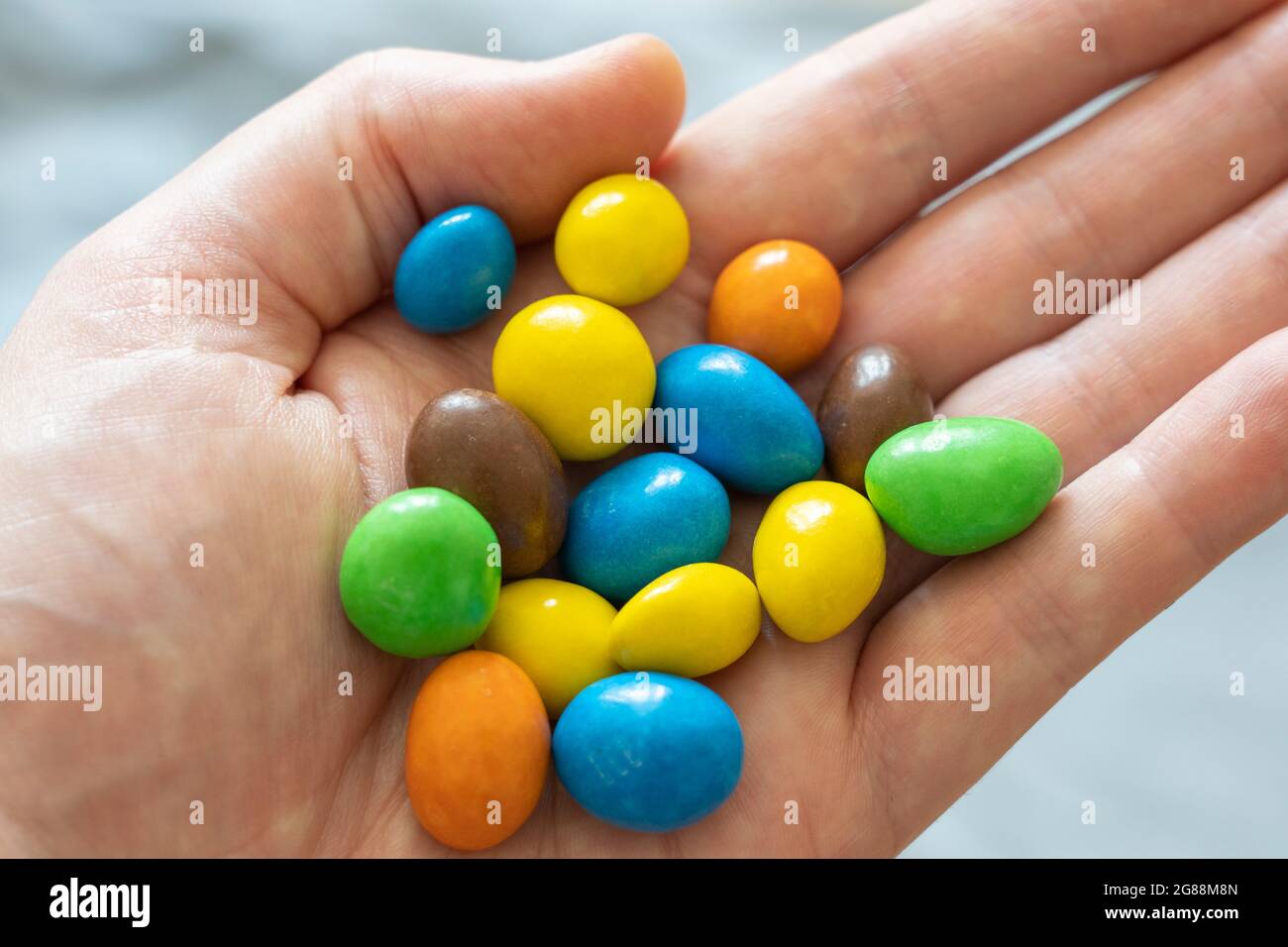 Una mano de hombre de 40 años con una selección de M&M de colores. Tema: Dieta azucarada, estilo de vida poco saludable, snacking poco saludable, alergia al maní Foto de stock